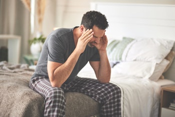 A man feeling stressed and suffering from a headache in bed at home. A mature guy looking unhappy, f...