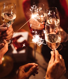 Champagne glasses clinking with sparklers, celebrating how each Zodiac sign makes New Year's resolut...