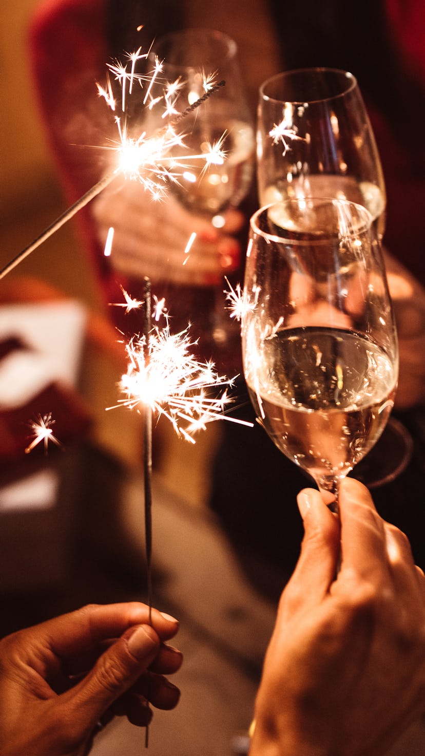 Champagne glasses clinking with sparklers, celebrating how each Zodiac sign makes New Year's resolut...