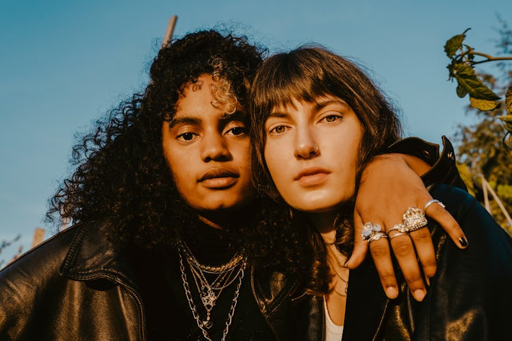 Two stylish young women wearing black with silver jewelry gaze into the camera in golden lighting, o...