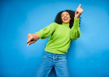 young woman dances and smiles in a green sweater as she considers how the january 2023 new moon will...