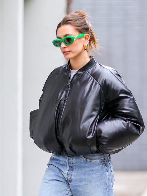Hailey Bieber wears a patent leather puffer coat and green sunglasses