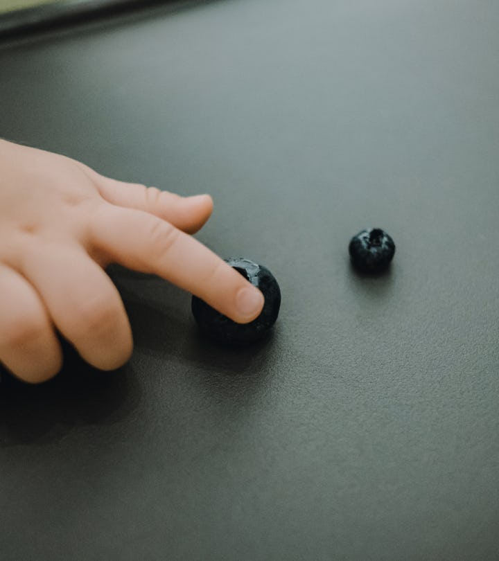 Close up of baby's hand making decision and picking up a bigger sized blueberry on high chair