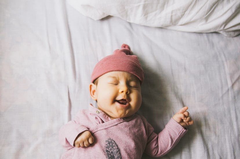 happy baby in pink beanie lying on bed for article on short unisex baby names