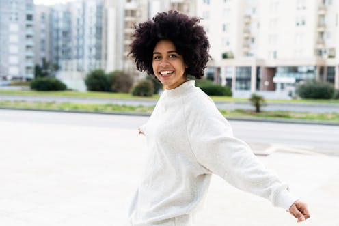 A young black African American woman dancing in the street while looking happy and smiling at the ca...