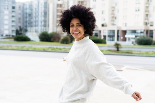 A young black African American woman dancing in the street while looking happy and smiling at the ca...