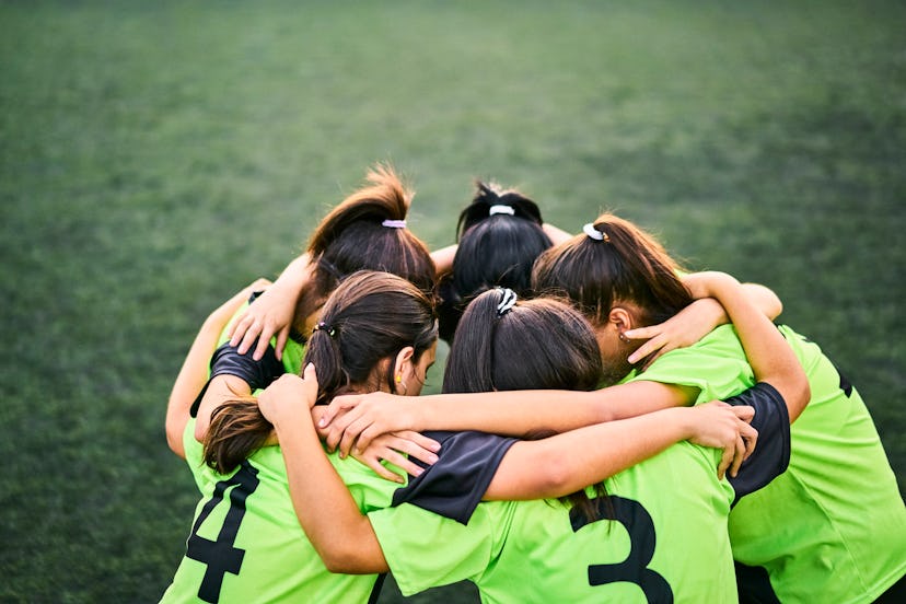High angle shot of team of soccer girls huddling on sports field before the match. Female players in...