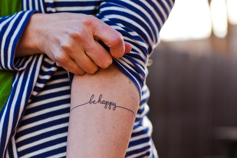 woman's arm with "be happy" on it as a tattoo, in a story about tattoos artists are tired of drawing...