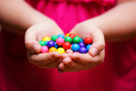 Young girl holding rainbow colored gum balls.