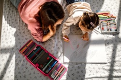 Mother and daughter having fun drawing with coloured pencils in a bedroom, lying down on a bed.