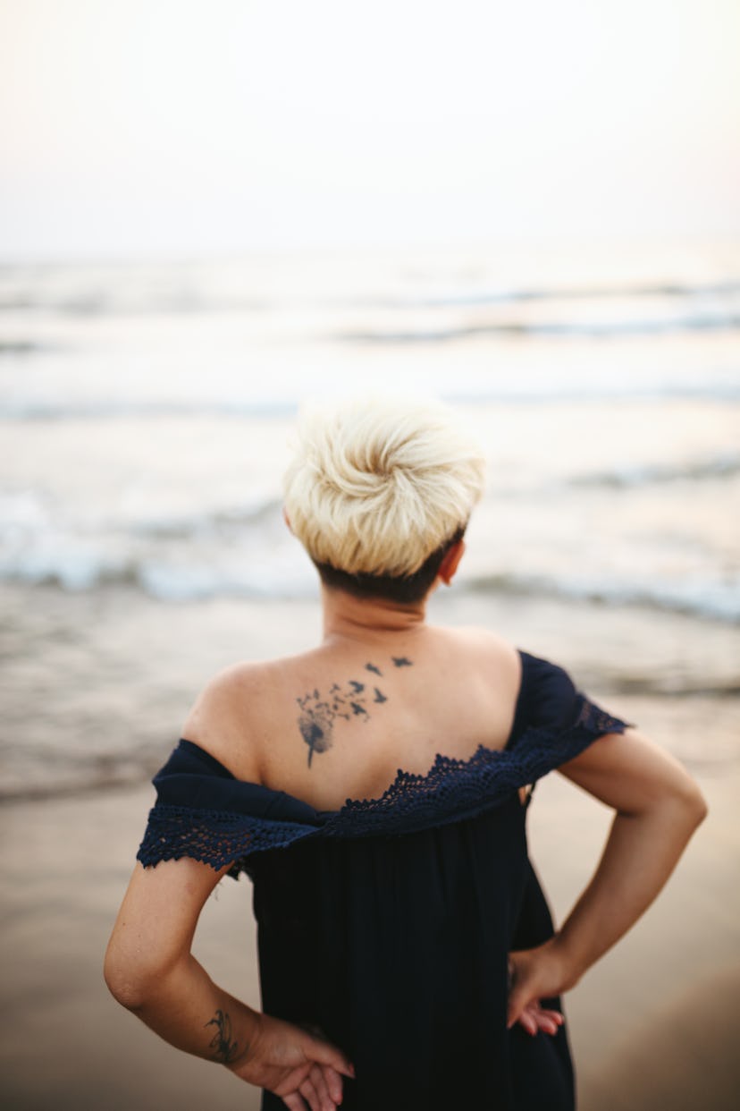 Young woman with dandelion tattoo on beach, in a story about tattoo designs artists are tired of.