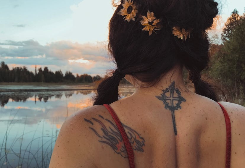 Behind view of a beautiful long haired woman, wearing a flower crown and sitting on a lake dock with...