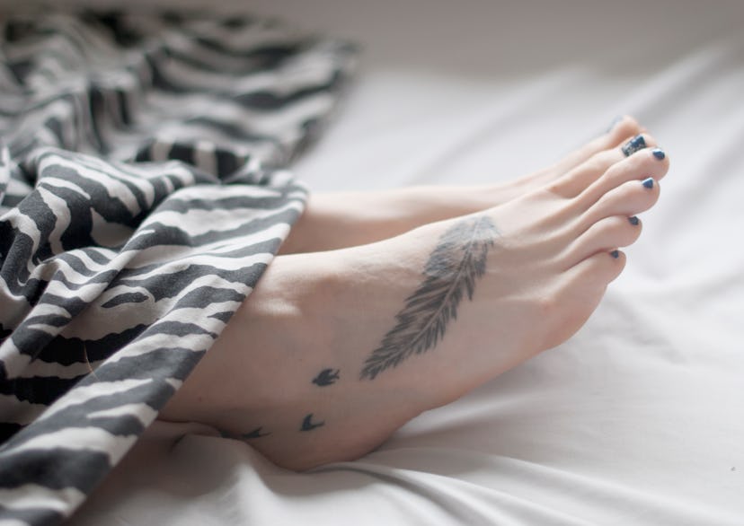 Womans foot amongst bed clothes with a feather tattoo and small birds, in a story about tattoo desig...