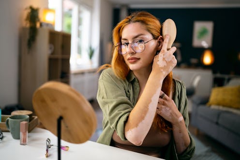 Modern young redhead Caucasian woman, with vitiligo and acne on her face, brushing her hair
