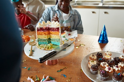 Multi colored cake on table while teenage girl sitting in background during birthday party, red dye ...