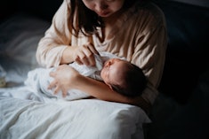 A mother sits in bed and wipes her baby's mouth with a muslin.