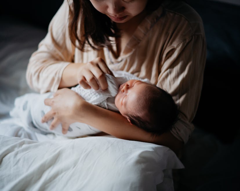 A mother sits in bed and wipes her baby's mouth with a muslin.