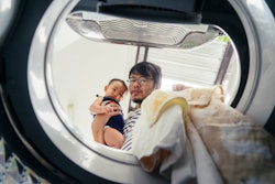 Dad holding baby, doing laundry; what to do if you run a disposable diaper in the wash