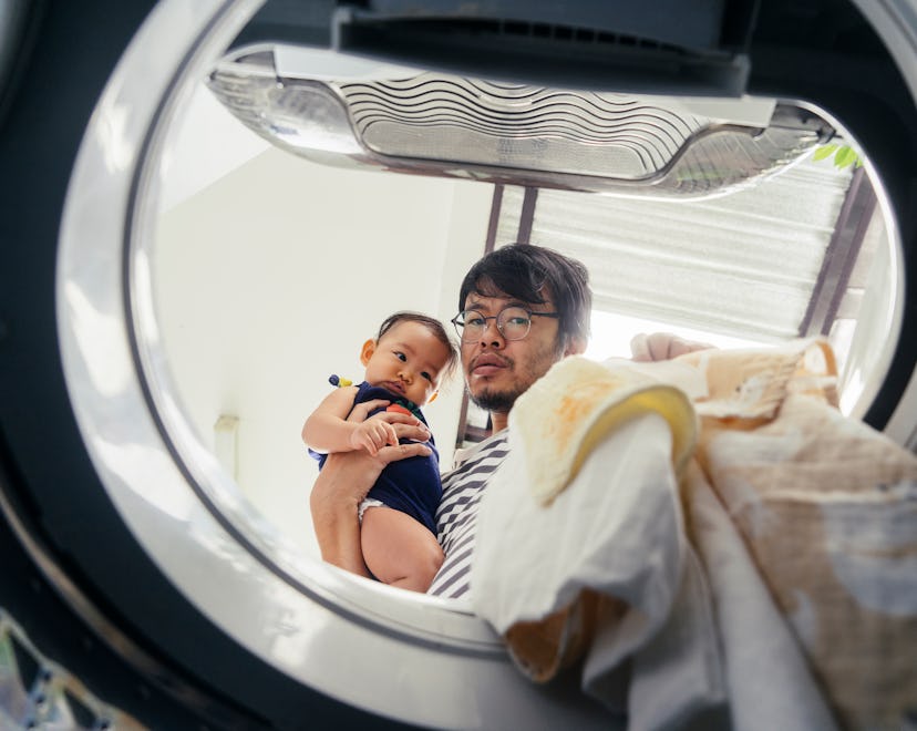 Dad holding baby, doing laundry; what to do if you run a disposable diaper in the wash