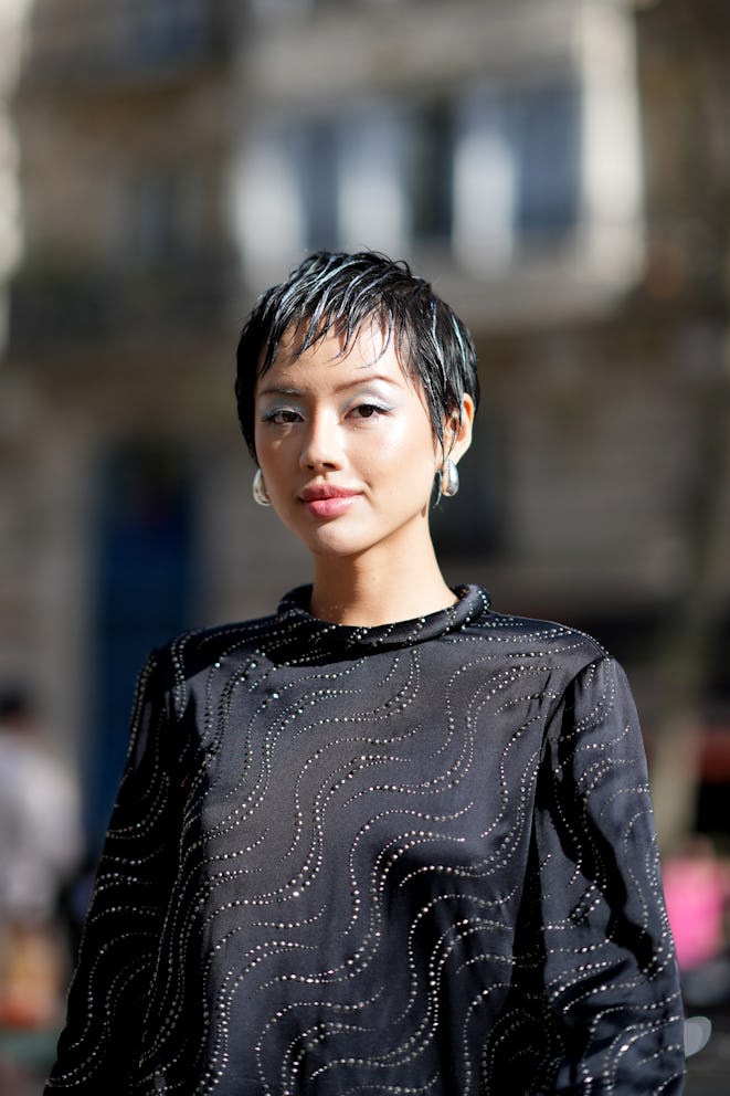 PARIS, FRANCE - OCTOBER 02: Khanh Linh wears earrings, a black lustrous silk mini dress with long sl...