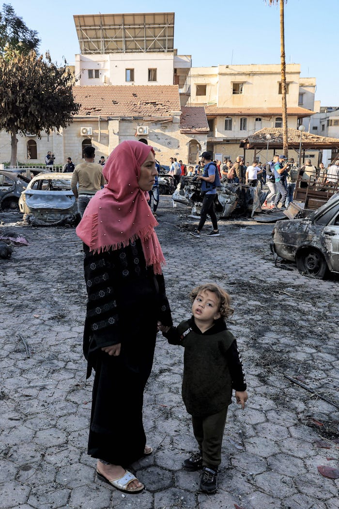 A woman stands with a girl outside the site of the Ahli Arab hospital in central Gaza on October 18,...