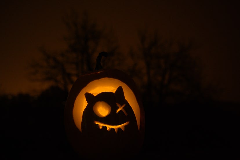 Winking Jack O' Lantern illuminated on Halloween night with the night sky and a spooky tree in the b...