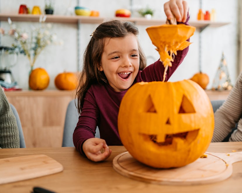 Young daughter carving out a pumpkin for Halloween while her parents are sitting next to her.