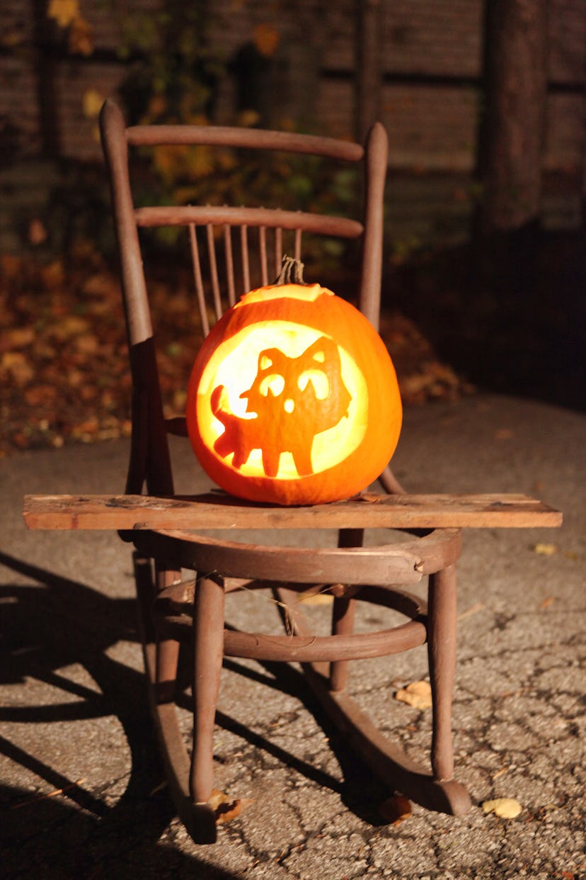 Jack-o'-lantern carved with the image of a cat rests on a wooden rocking chair during Halloween nigh...