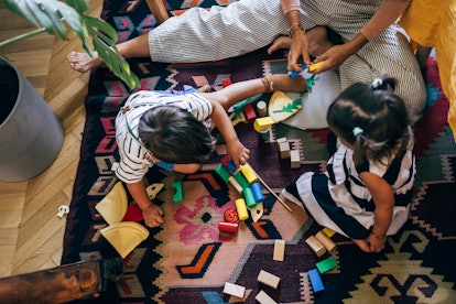 Above shot of a family playing with wooden building blocks on the floor of a bedroom, in a story abo...