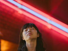A portrait of a young woman with her eyes closed in front of neon lights as she reflects on how the ...
