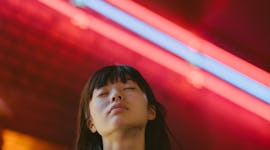 A portrait of a young woman with her eyes closed in front of neon lights as she reflects on how the ...
