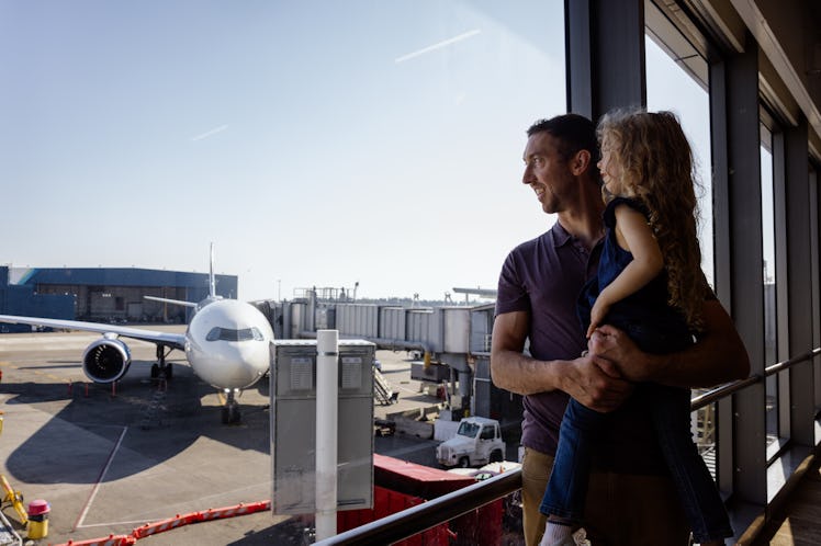 A father and daughter traveling together at an airport, waiting to board their plane. They look out...