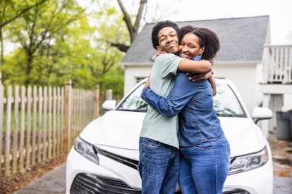 Portrait of single mother and teenage boy holding keys in front of his first car