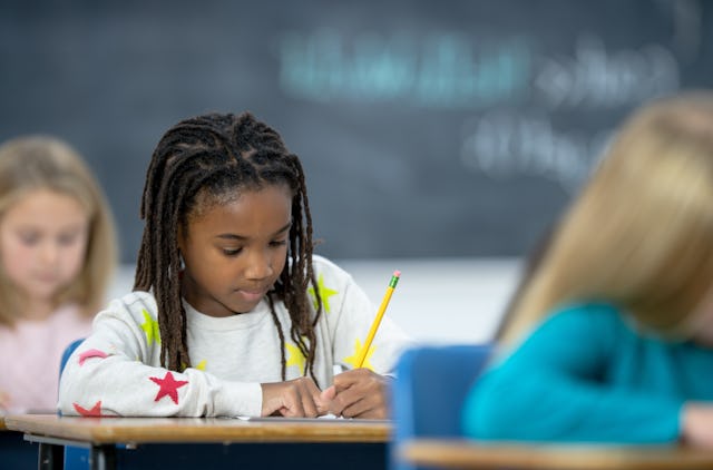 A group of multi-ethnic elementary students each sit at their desks in class with pencils inn hands ...