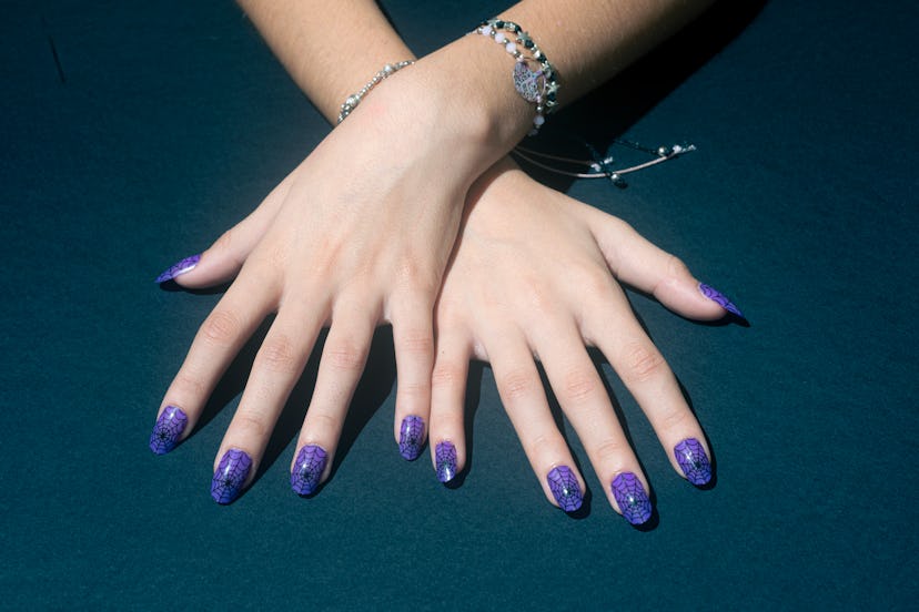 Female hands with false nails with drawn cobwebs on a blue background.Nail Art Manicure halloween na...