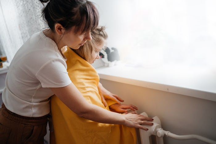 mother and child are warming themselves near the radiator by the window of the house