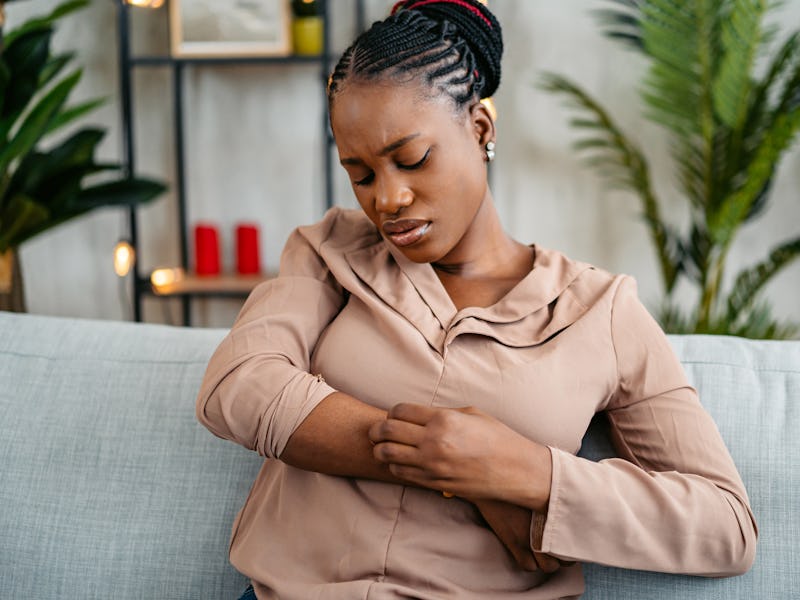 Young black woman having a rash (skin condition) while sitting on the sofa at home.