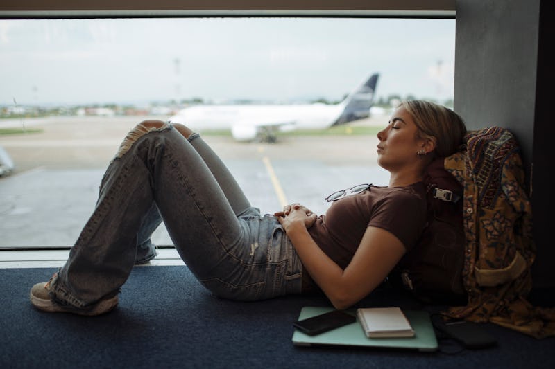Young woman taking a nap on the airport floor while waiting for her flight