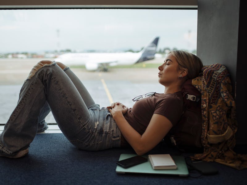 Young woman taking a nap on the airport floor while waiting for her flight