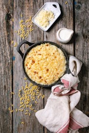 Classic american dish baked mac and cheese in cast iron pan with kitchen towel and ingredients above...