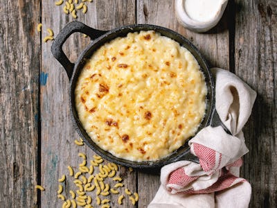 Classic american dish baked mac and cheese in cast iron pan with kitchen towel and ingredients above...