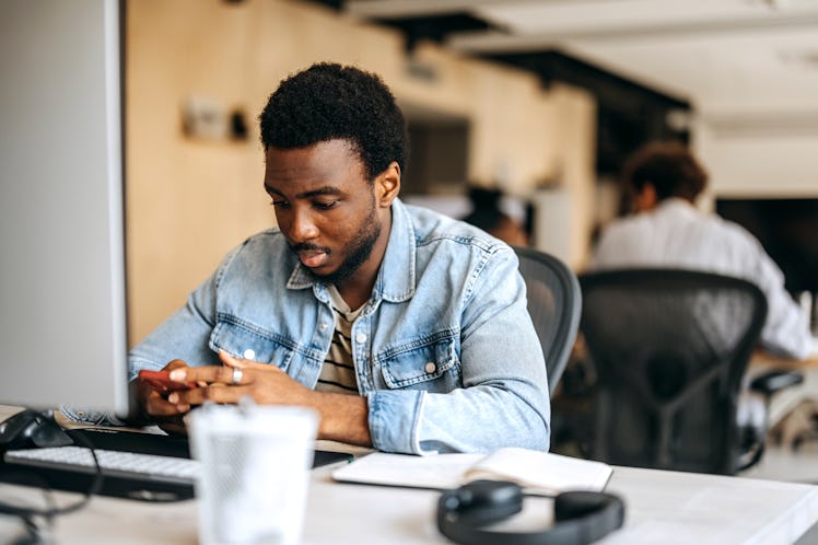 Young casually clothed man using phone at modern office