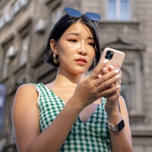 Worried Chinese woman surfing the Internet on mobile phone while standing on the street.