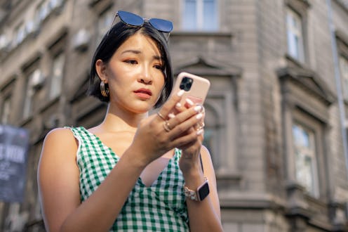 Worried Chinese woman surfing the Internet on mobile phone while standing on the street.