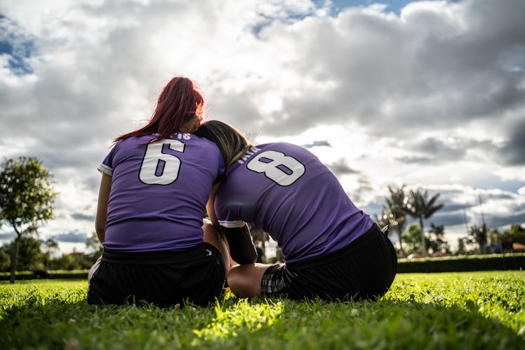 Rear view of female soccer players sitting on ground outdoors