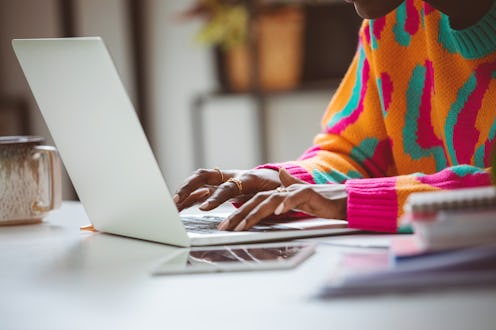 Afro american young woman wearing colorful sweater sitting at the desk at home and using laptop. Clo...