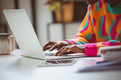 Afro american young woman wearing colorful sweater sitting at the desk at home and using laptop. Clo...
