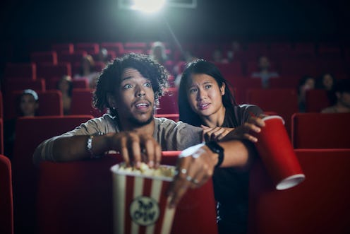 Fearful diverse couple watching a crime movie in cinema. Focus is on black man.
