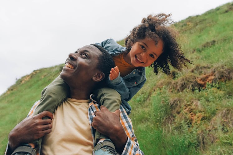 Black dad and daughter are having fun. A little girl sits on dad's shoulders.