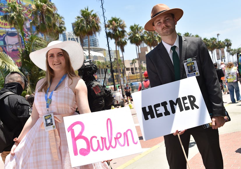 Cosplayers hold Barbenheimer signs outside the convention center during San Diego Comic-Con Internat...